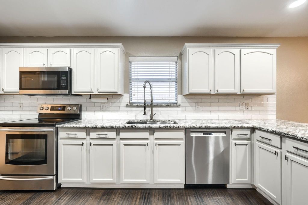 Kitchen with stainless steel appliances, white cabinetry, light stone counters, decorative backsplash, and dark wood-style floors