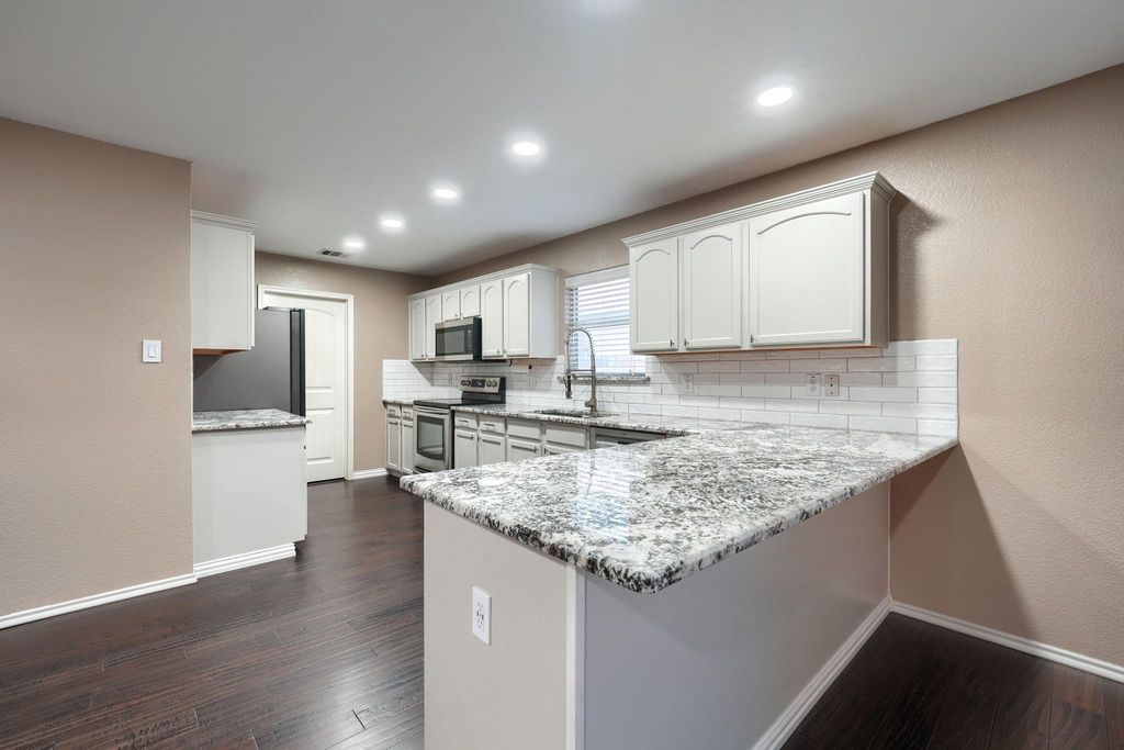 Kitchen with light stone counters, a peninsula, white cabinetry, dark wood-style floors, and stainless steel appliances