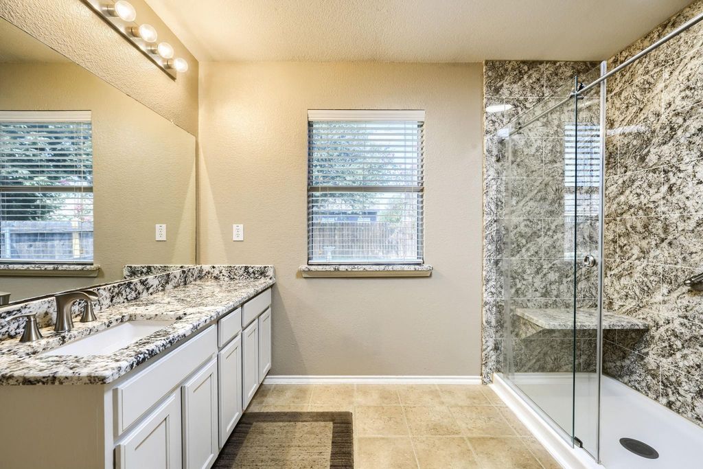 Bathroom with double vanity, a shower stall, a textured wall, light tile patterned floors, and a textured ceiling