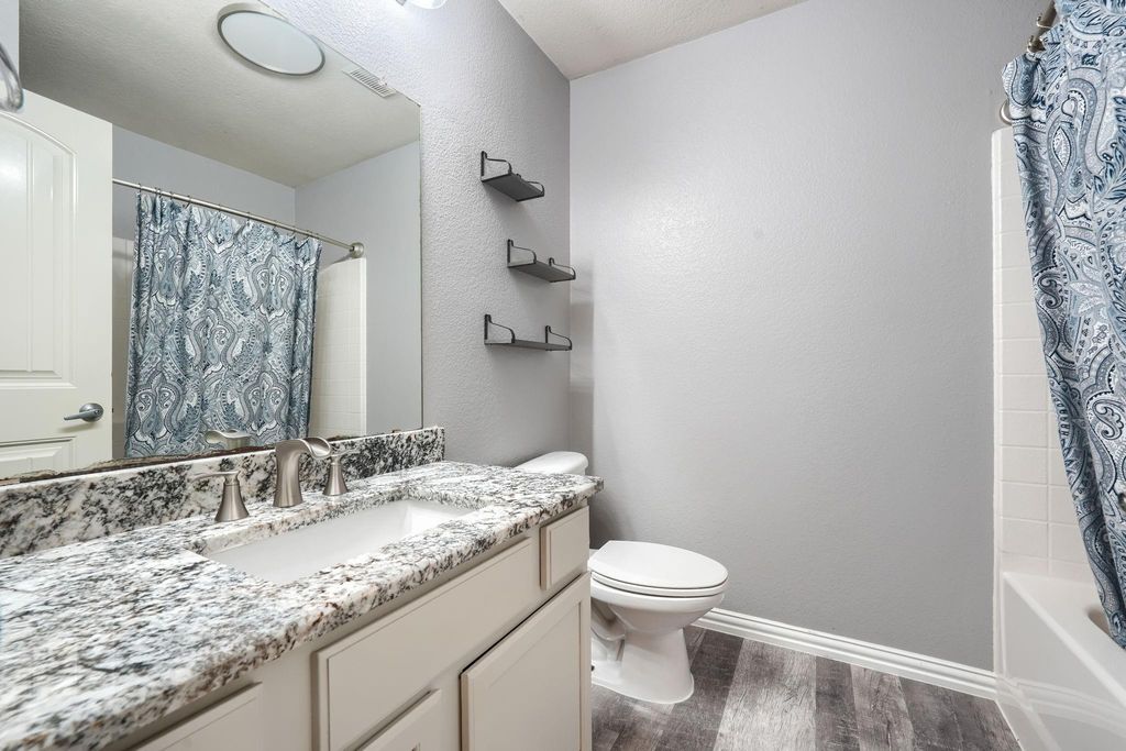 Full bathroom featuring dark wood-style flooring, vanity, shower / bath combo with shower curtain, and a textured wall