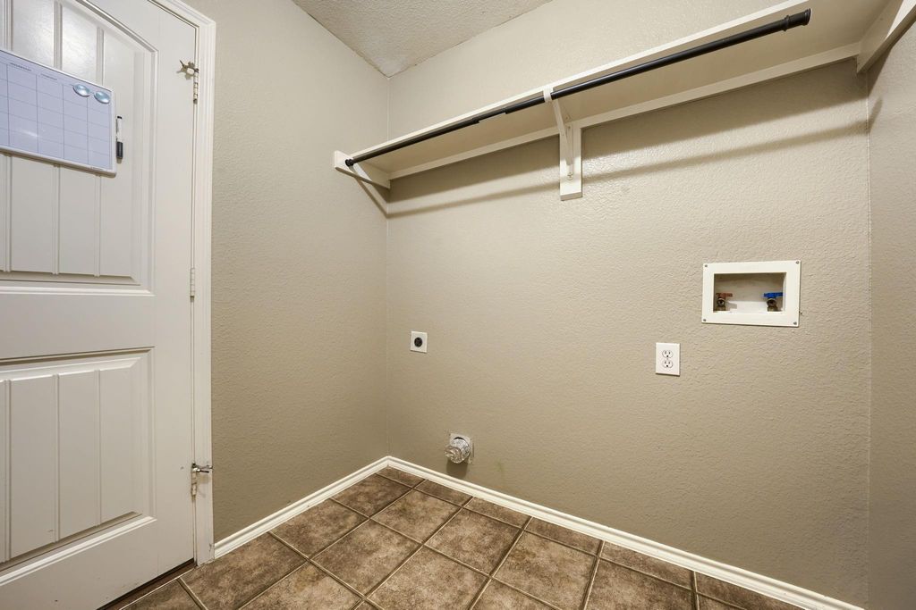 Washroom featuring hookup for an electric dryer, a textured wall, hookup for a washing machine, and tile patterned flooring