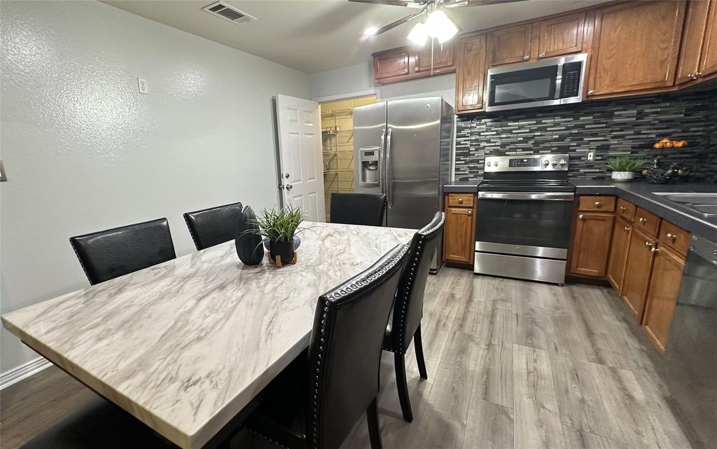 Kitchen with stainless steel appliances, brown cabinets, dark countertops, tasteful backsplash, and light wood-type flooring