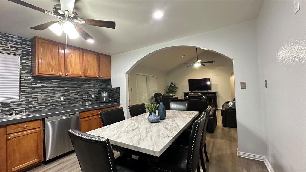 Kitchen with arched walkways, a ceiling fan, brown cabinets, tasteful backsplash, and open floor plan