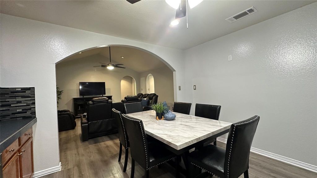 Dining area featuring a ceiling fan, lofted ceiling, dark wood-style flooring, arched walkways, and a textured wall