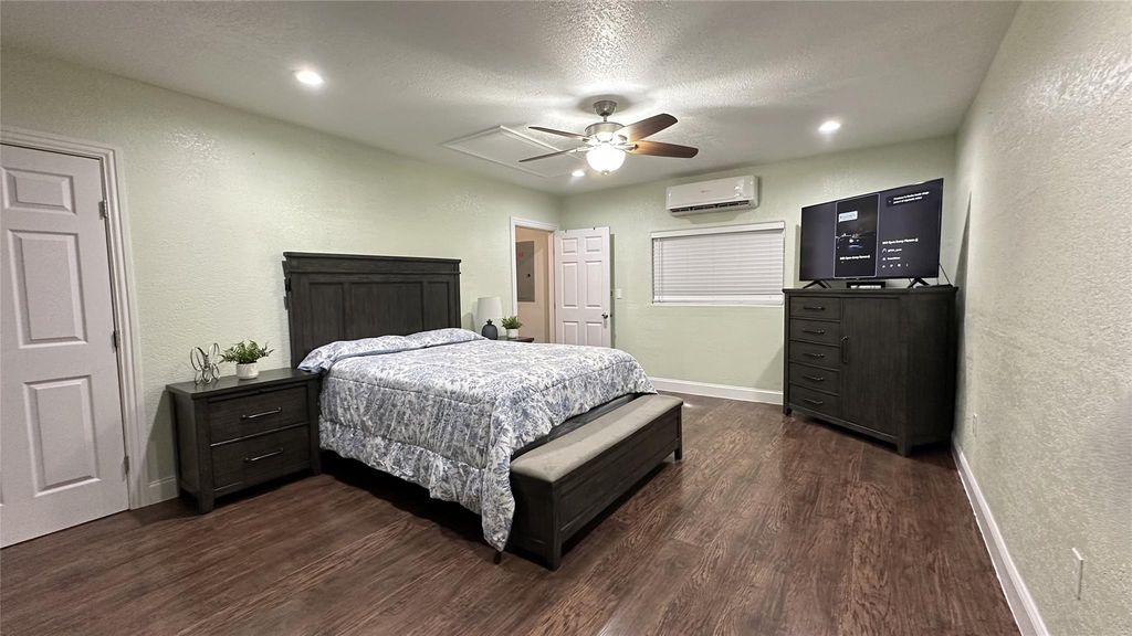 Bedroom featuring a textured wall, dark wood-type flooring, a textured ceiling, a ceiling fan, and a wall unit AC