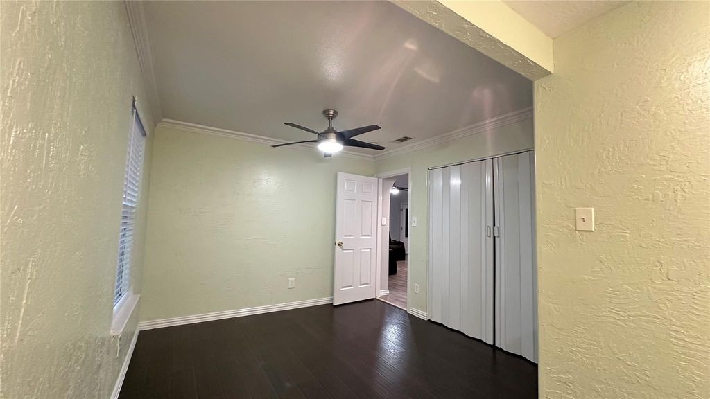 Unfurnished bedroom with a textured wall, crown molding, dark wood-style floors, a closet, and ceiling fan