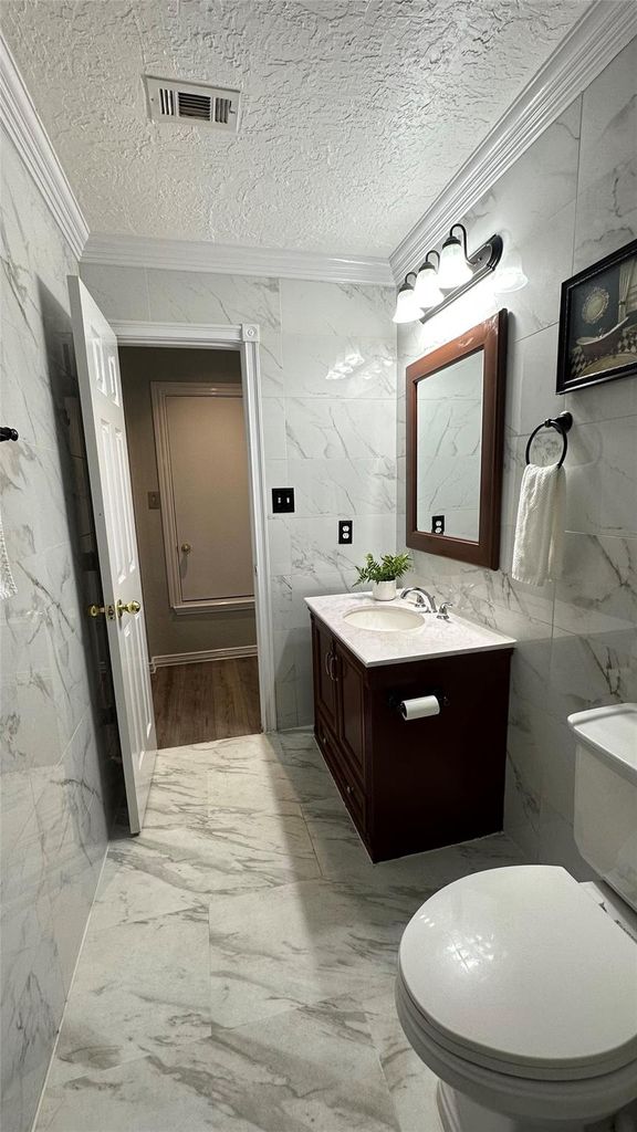 Half bathroom featuring light marble finish flooring, tile walls, vanity, a textured ceiling, and crown molding