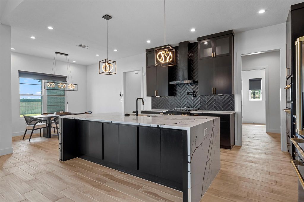 Kitchen featuring dark cabinets, light stone counters, pendant lighting, recessed lighting, and light wood finished floors