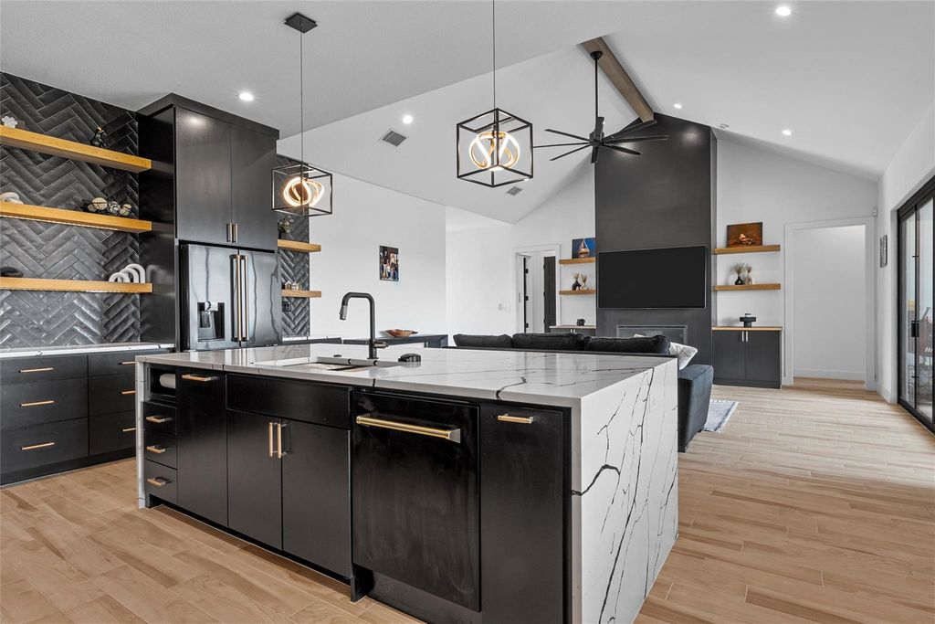Kitchen featuring dark cabinetry, beamed ceiling, open shelves, hanging light fixtures, and open floor plan