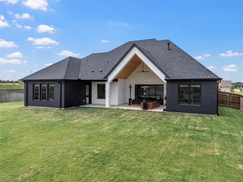 Back of house featuring brick siding, a patio, and roof with shingles
