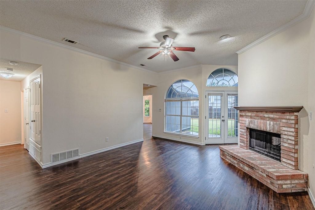 Unfurnished living room featuring crown molding, a textured ceiling, dark wood finished floors, french doors, and a brick fireplace