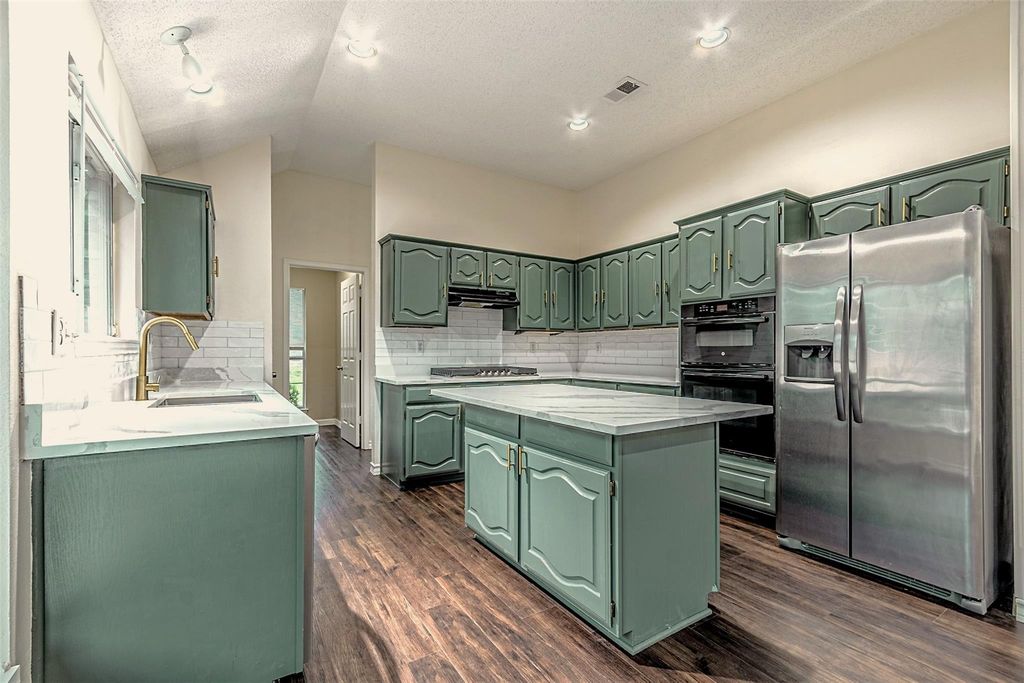 Kitchen with green cabinetry, stainless steel fridge with ice dispenser, a center island, backsplash, and a textured ceiling