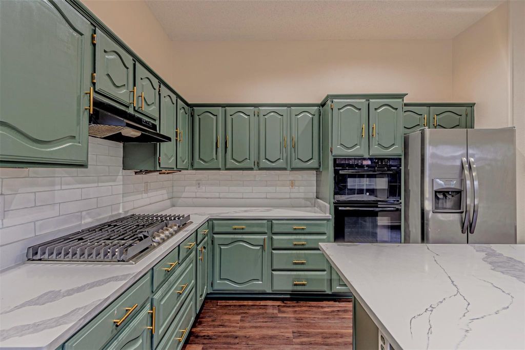 Kitchen with green cabinetry, light stone countertops, and stainless steel appliances