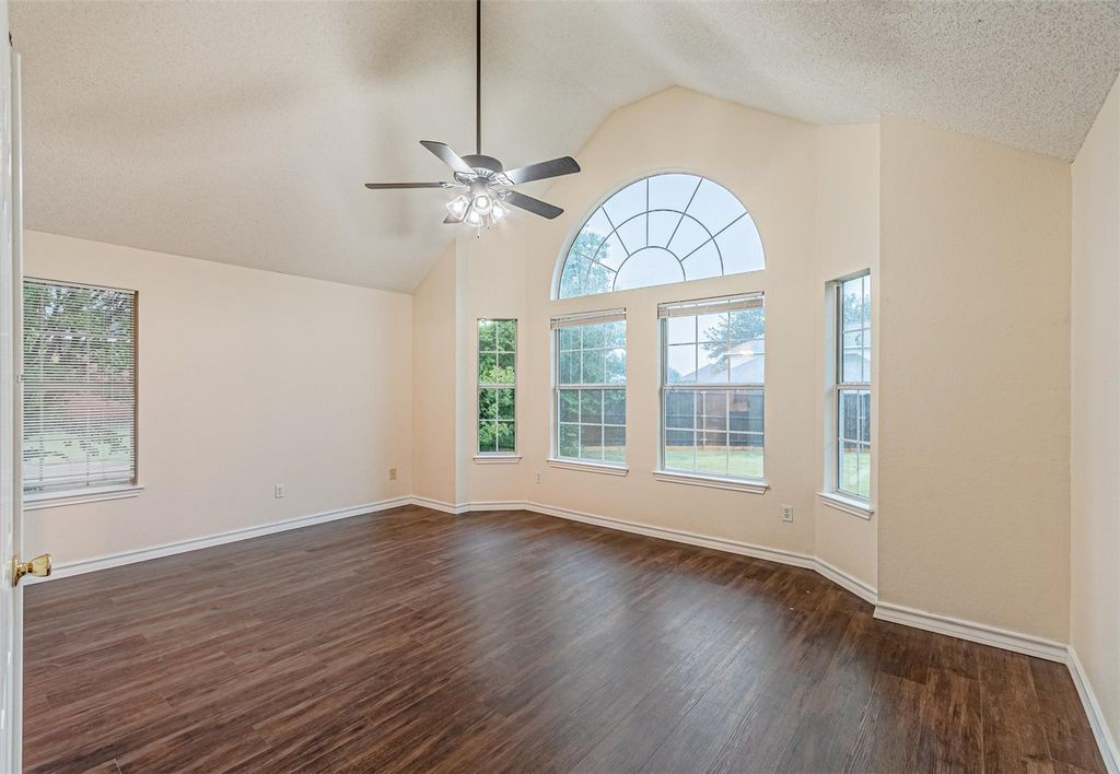 Empty room with dark wood-style floors, high vaulted ceiling, a ceiling fan, and a textured ceiling