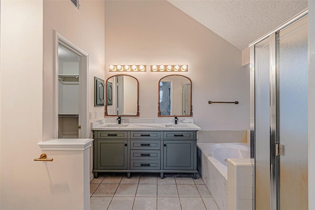 Bathroom featuring double vanity, light tile patterned floors, a garden tub, a textured ceiling, and lofted ceiling