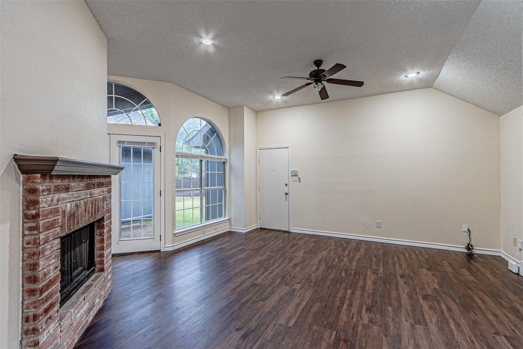 Unfurnished living room featuring a textured ceiling, dark wood-style flooring, vaulted ceiling, a fireplace, and a ceiling fan