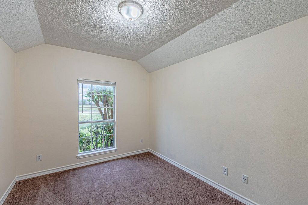 Carpeted empty room with vaulted ceiling and a textured ceiling
