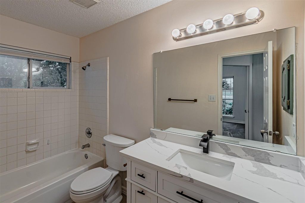 Full bathroom featuring shower / bathtub combination, plenty of natural light, vanity, and a textured ceiling
