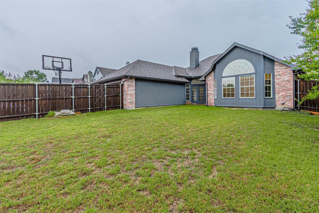 Rear view of property with a fenced backyard, brick siding, a chimney, and roof with shingles
