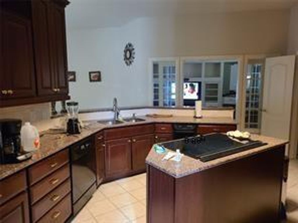 Kitchen featuring dark brown cabinetry, a peninsula, light stone countertops, and black appliances