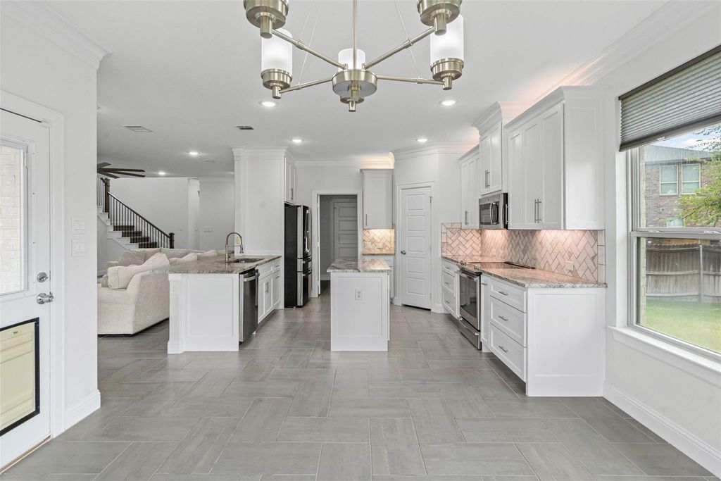 Kitchen with open floor plan, crown molding, backsplash, appliances with stainless steel finishes, and light stone counters