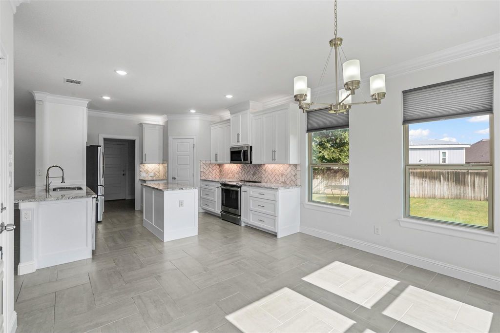 Kitchen with crown molding, backsplash, white cabinets, appliances with stainless steel finishes, and hanging light fixtures
