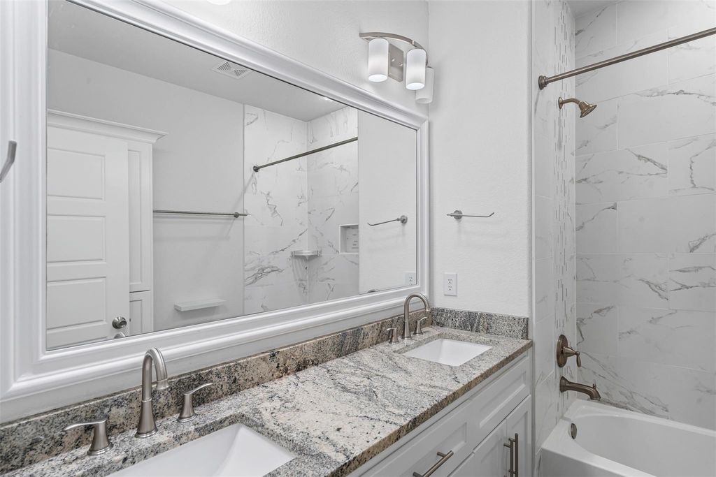 Full bathroom featuring a combined bath / shower with marble appearance and double vanity