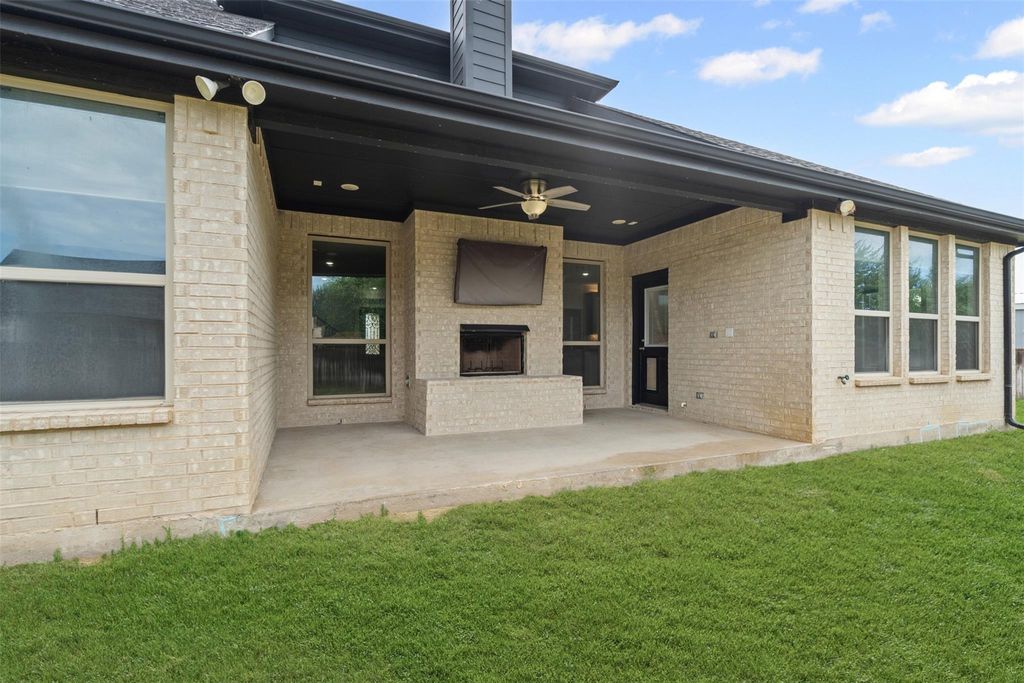 Back of property featuring brick siding, a ceiling fan, an outdoor brick fireplace, a patio area, and a lawn
