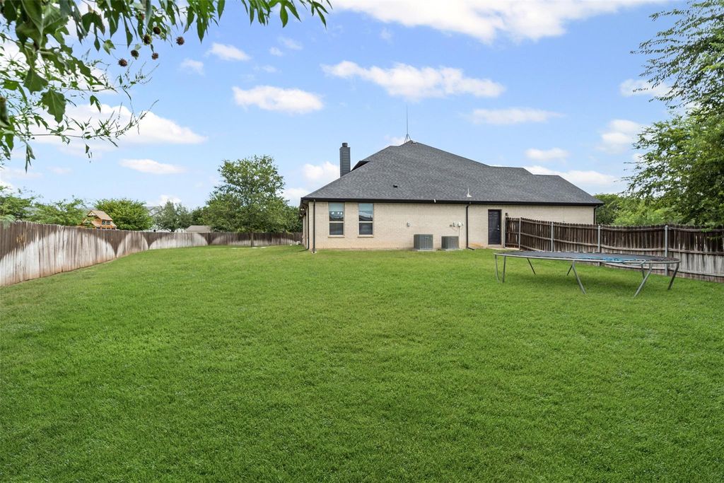 Back of property with a chimney, a fenced backyard, brick siding, and a trampoline