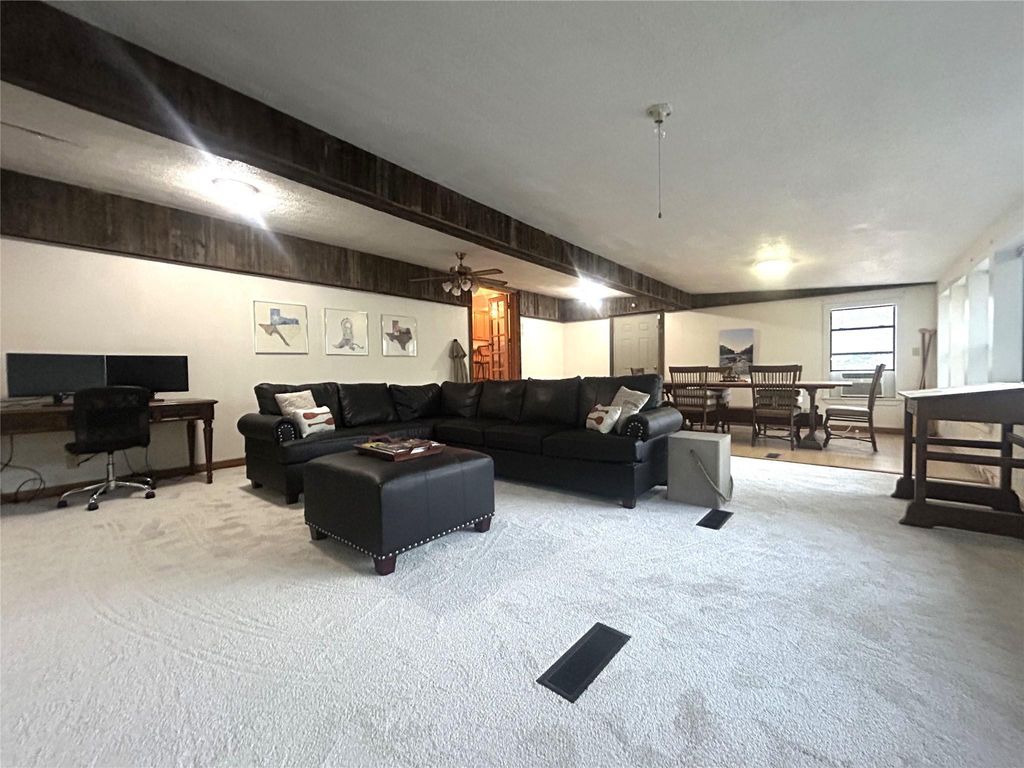 Carpeted living area featuring a desk, a ceiling fan, and beamed ceiling