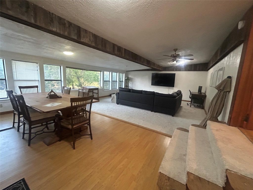 Dining space featuring wood finished floors, a textured ceiling, ceiling fan, and beamed ceiling