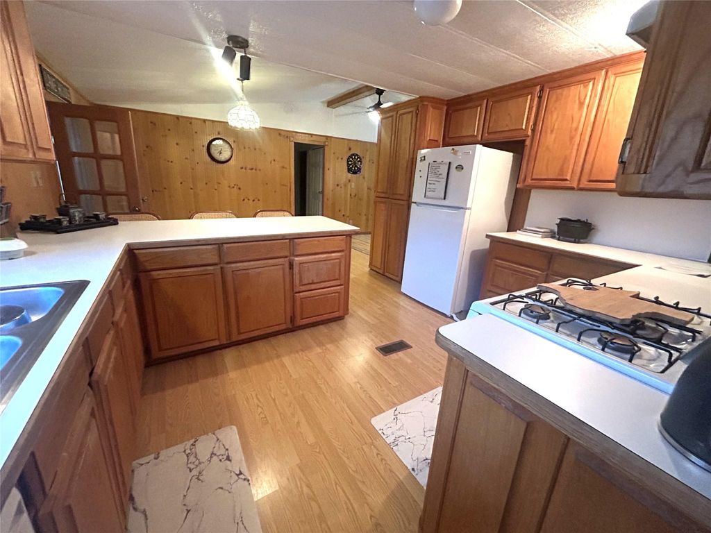 Kitchen with brown cabinetry, light countertops, freestanding refrigerator, light wood finished floors, and hanging light fixtures