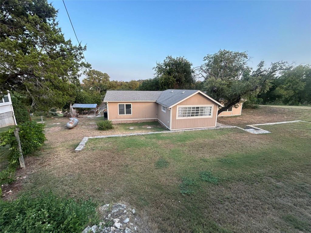 View of front of property with a front lawn, roof with shingles, and view of wooded area