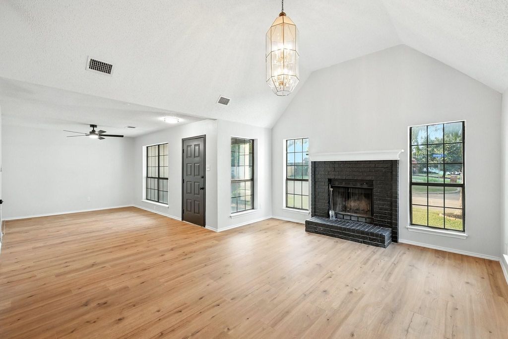 Unfurnished living room featuring light wood-style floors, high vaulted ceiling, a brick fireplace, a chandelier, and ceiling fan