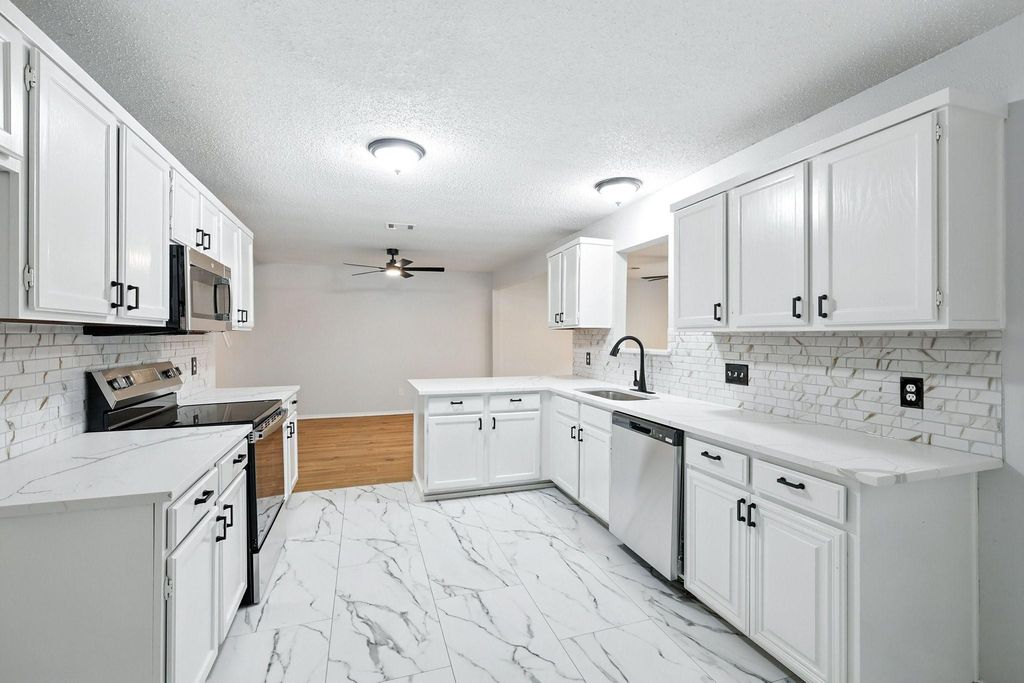 Kitchen with quartz countertops, decorative backsplash, stainless steel appliances, white cabinetry, a peninsula, and a textured ceiling