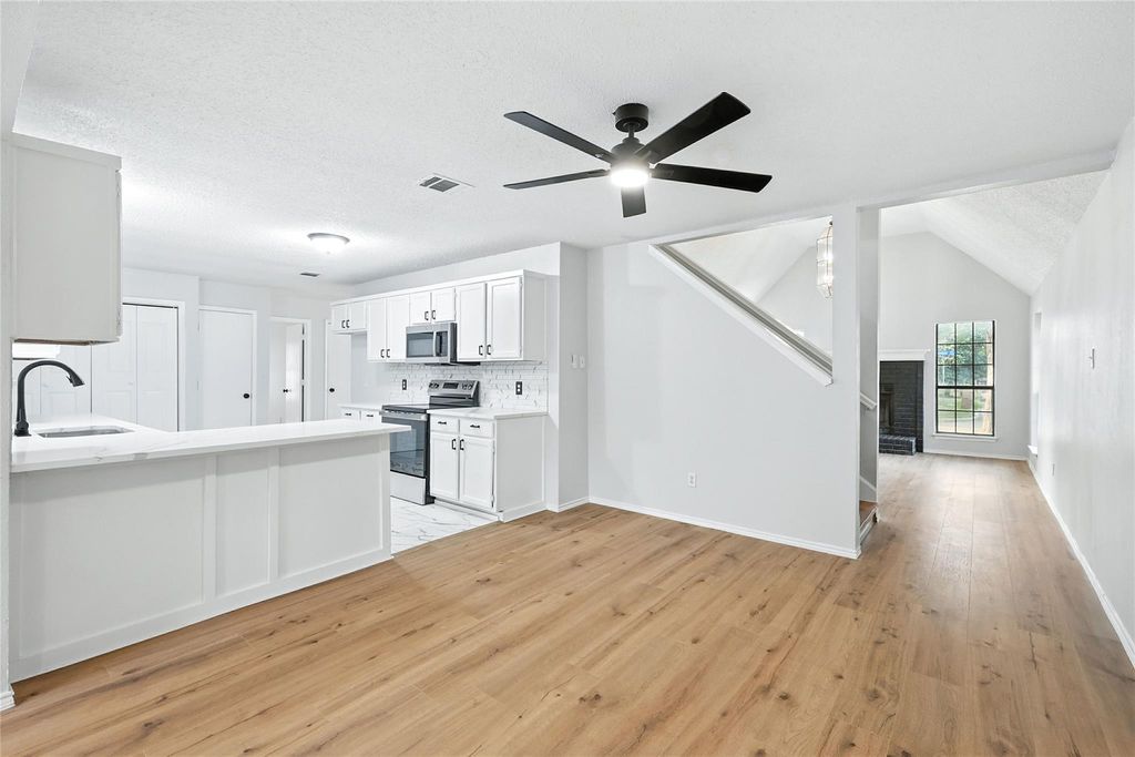 Kitchen featuring quartz countertops, stainless steel appliances, white cabinetry, backsplash, light wood-style floors, and ceiling fan