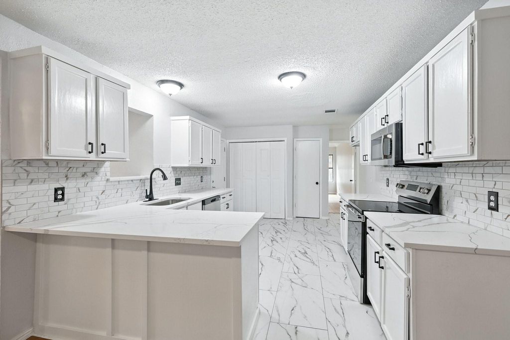 Kitchen featuring quartz countertops, a peninsula, appliances with stainless steel finishes, tasteful backsplash, white cabinets, and a textured ceiling