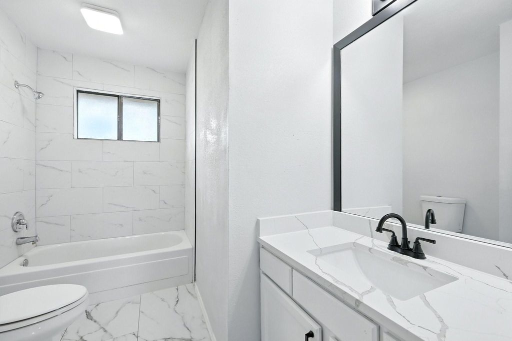 Full bath with quartz sink top, marble look tiles,  shower combination, and vanity