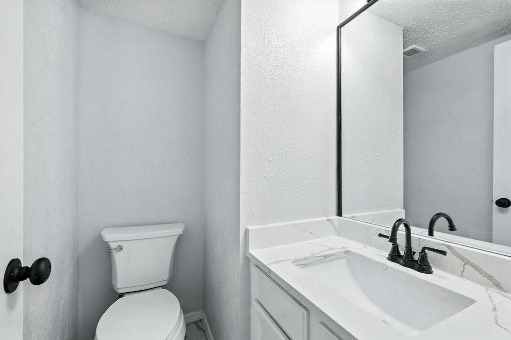 Bathroom featuring vanity, quartz countertop, a textured ceiling, and a textured wall