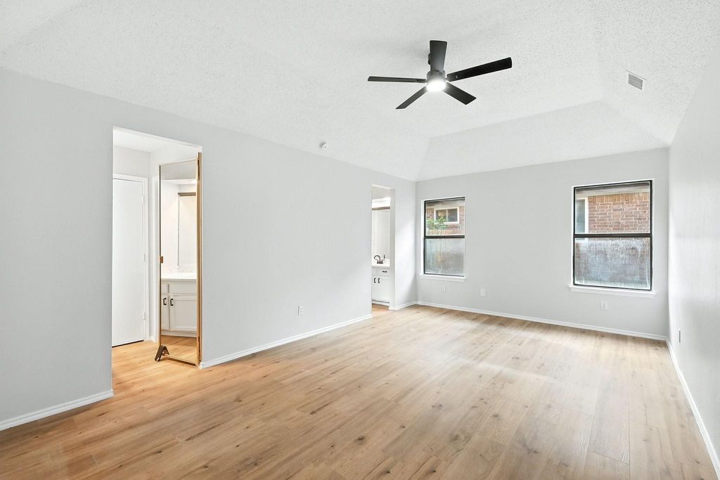 Unfurnished primary suite featuring a textured ceiling, light wood-style flooring, ensuite bath, ceiling fan, and a raised ceiling