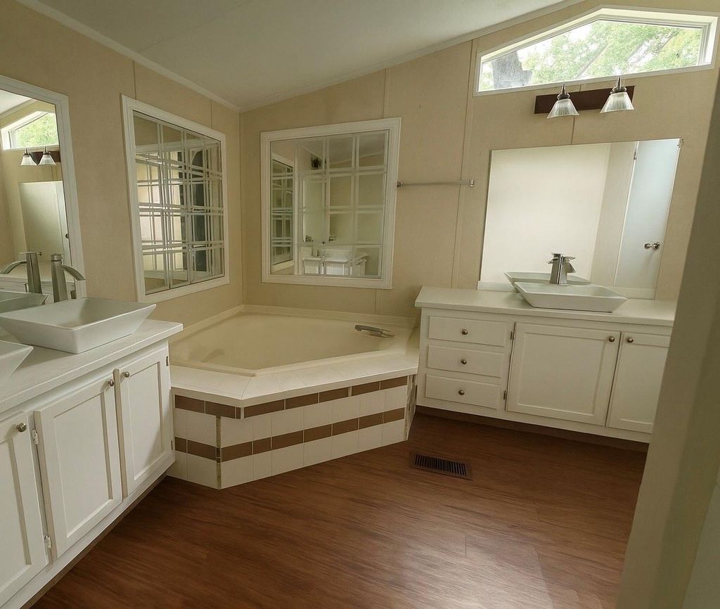 Full bath with two vanities, vaulted ceiling, a bath, and dark wood-style floors