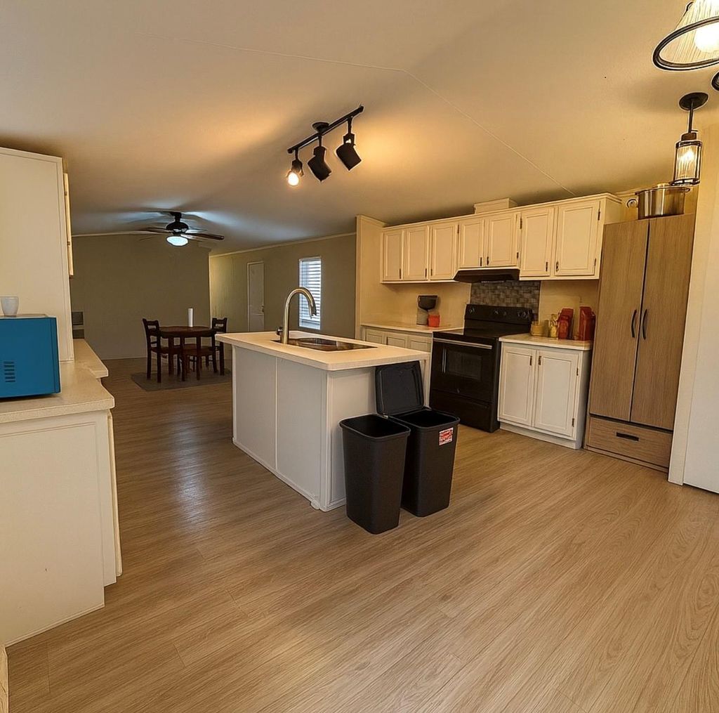 Kitchen with electric range, light wood-style flooring, light countertops, white cabinetry, and a ceiling fan