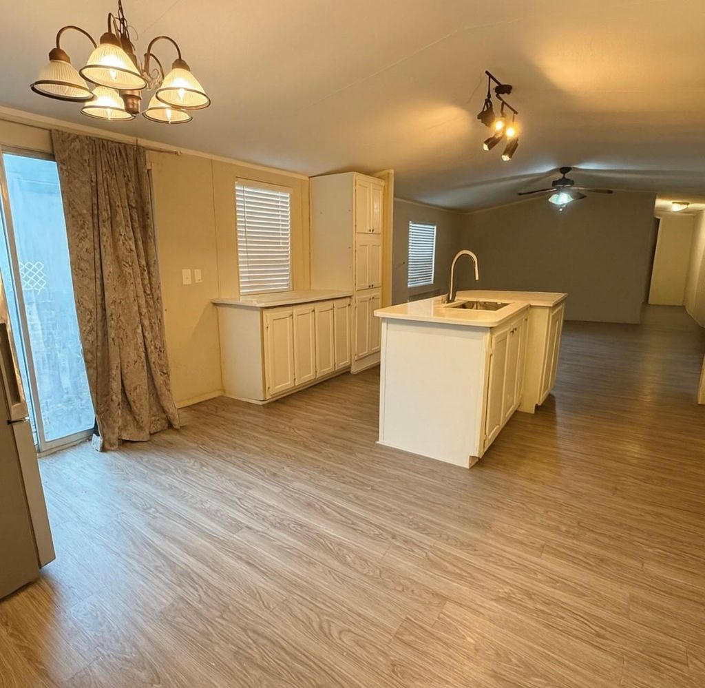 Kitchen with light wood-style floors, vaulted ceiling, healthy amount of natural light, and a kitchen island with sink