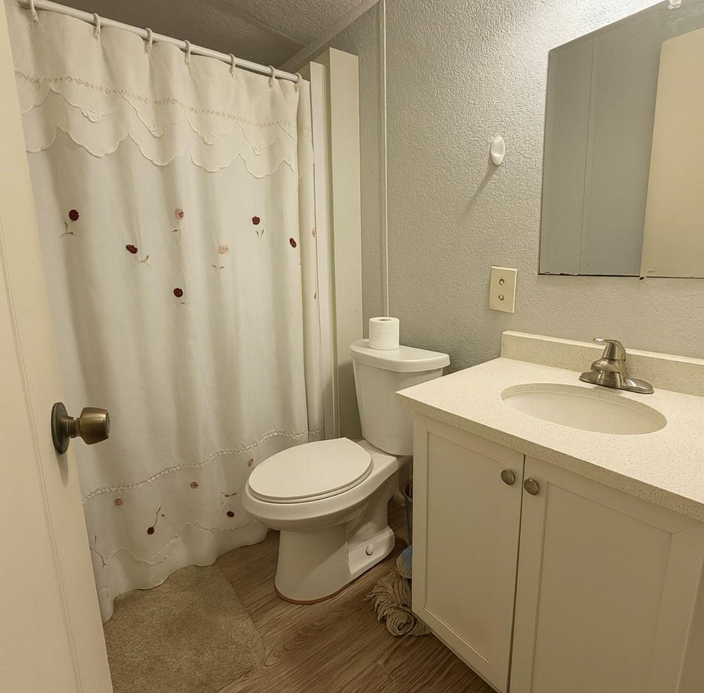 Full bathroom with a textured wall, vanity, light wood finished floors, and a shower with curtain