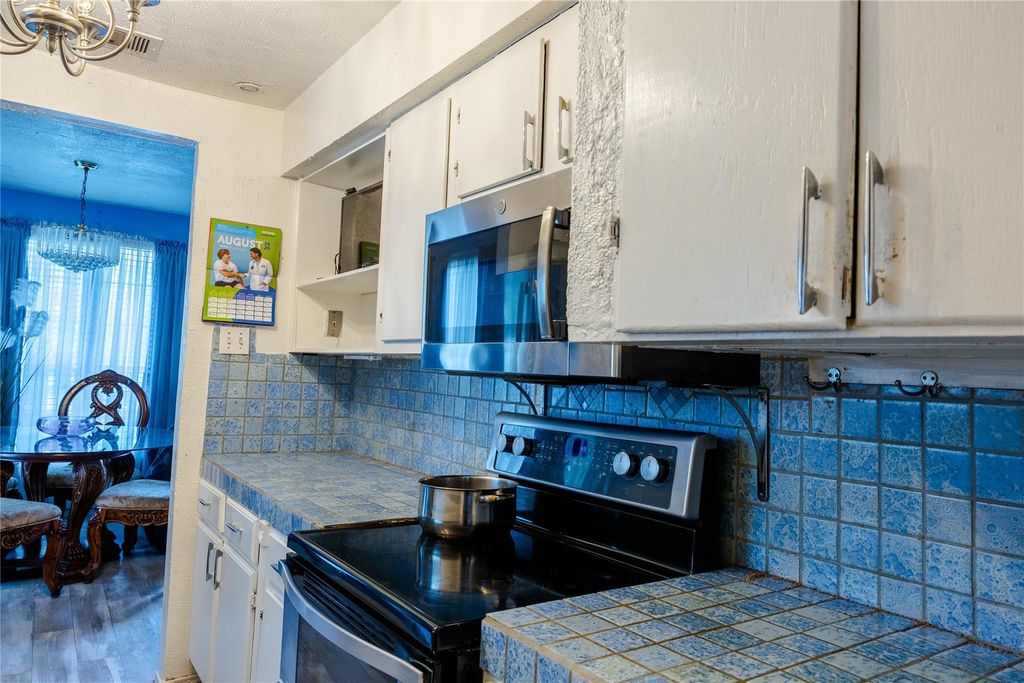 Kitchen with stainless steel electric stove, white cabinetry, tasteful backsplash, and decorative light fixtures