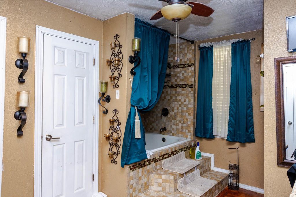 Bathroom with tiled shower / bath combo, a textured wall, and ceiling fan