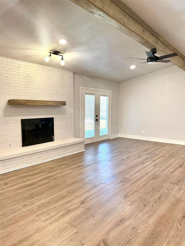 Unfurnished living room with a fireplace, french doors, wood finished floors, a ceiling fan, and a textured ceiling
