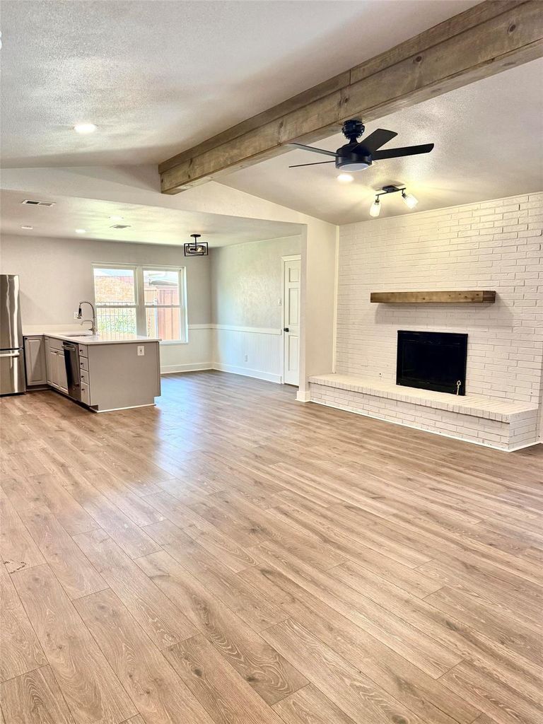 Unfurnished living room with a wainscoted wall, a textured ceiling, ceiling fan, light wood-style floors, and a fireplace