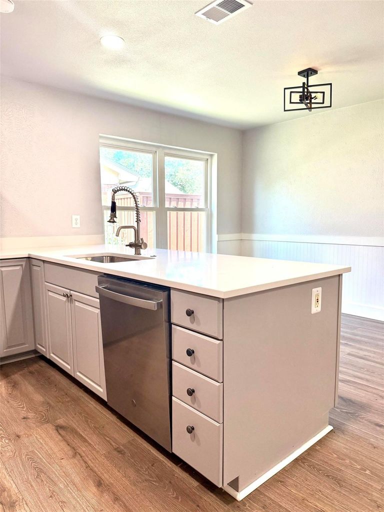 Kitchen featuring stainless steel dishwasher, light wood-type flooring, a peninsula, a wainscoted wall, and a textured ceiling