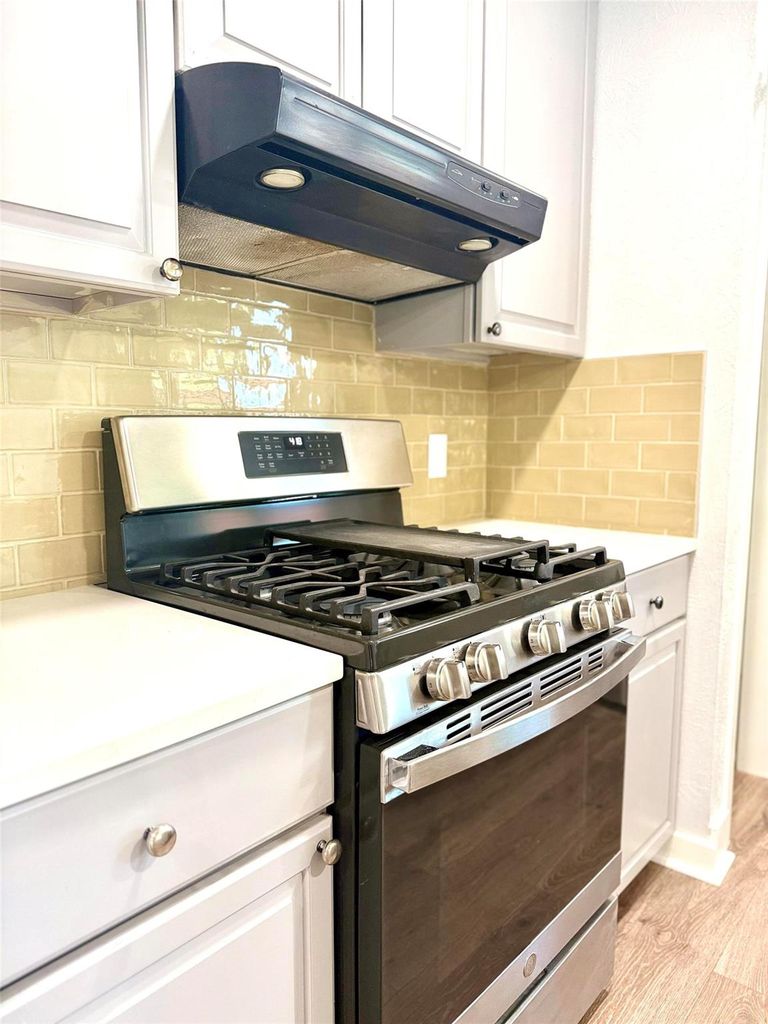 Kitchen with stainless steel range with gas stovetop, white cabinetry, under cabinet range hood, and backsplash